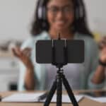 cell phone on tripod with woman shown behind camera recording video